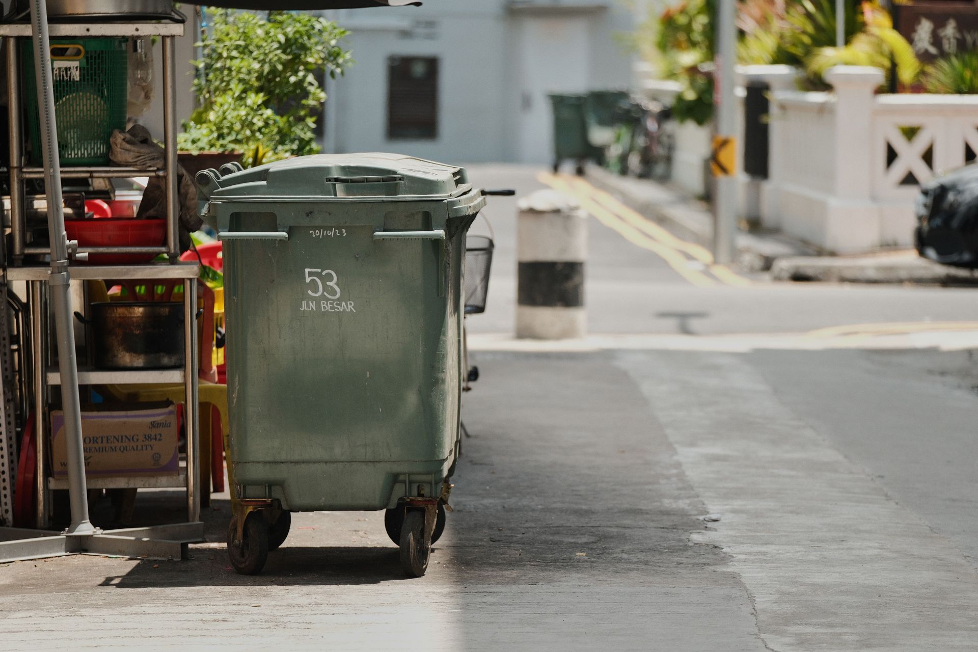 A green garbage bin on a quiet urban street under the sunlight.
