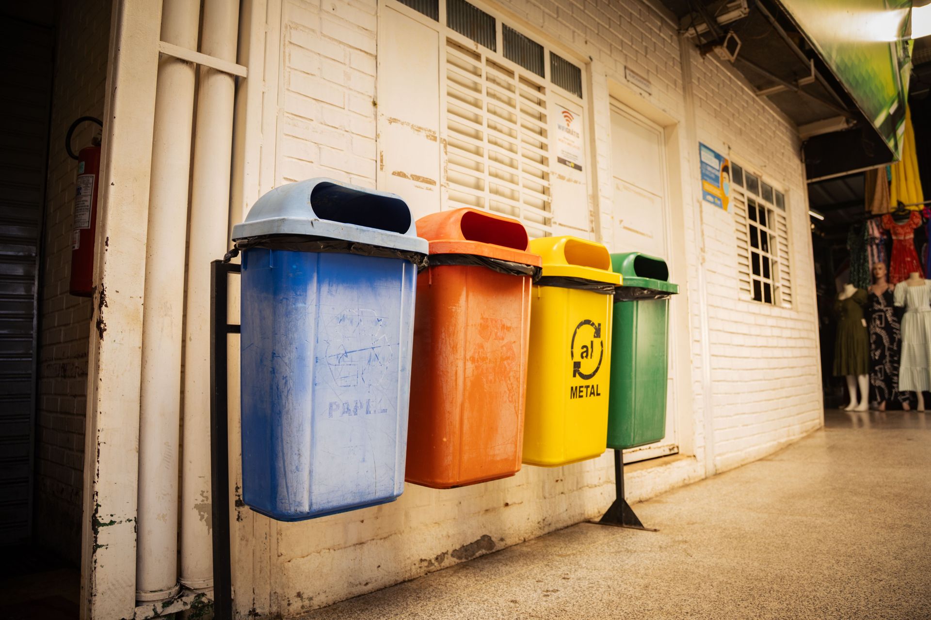 Four recycling bins for different materials in a market setting, emphasizing waste sorting and environmental awareness.
