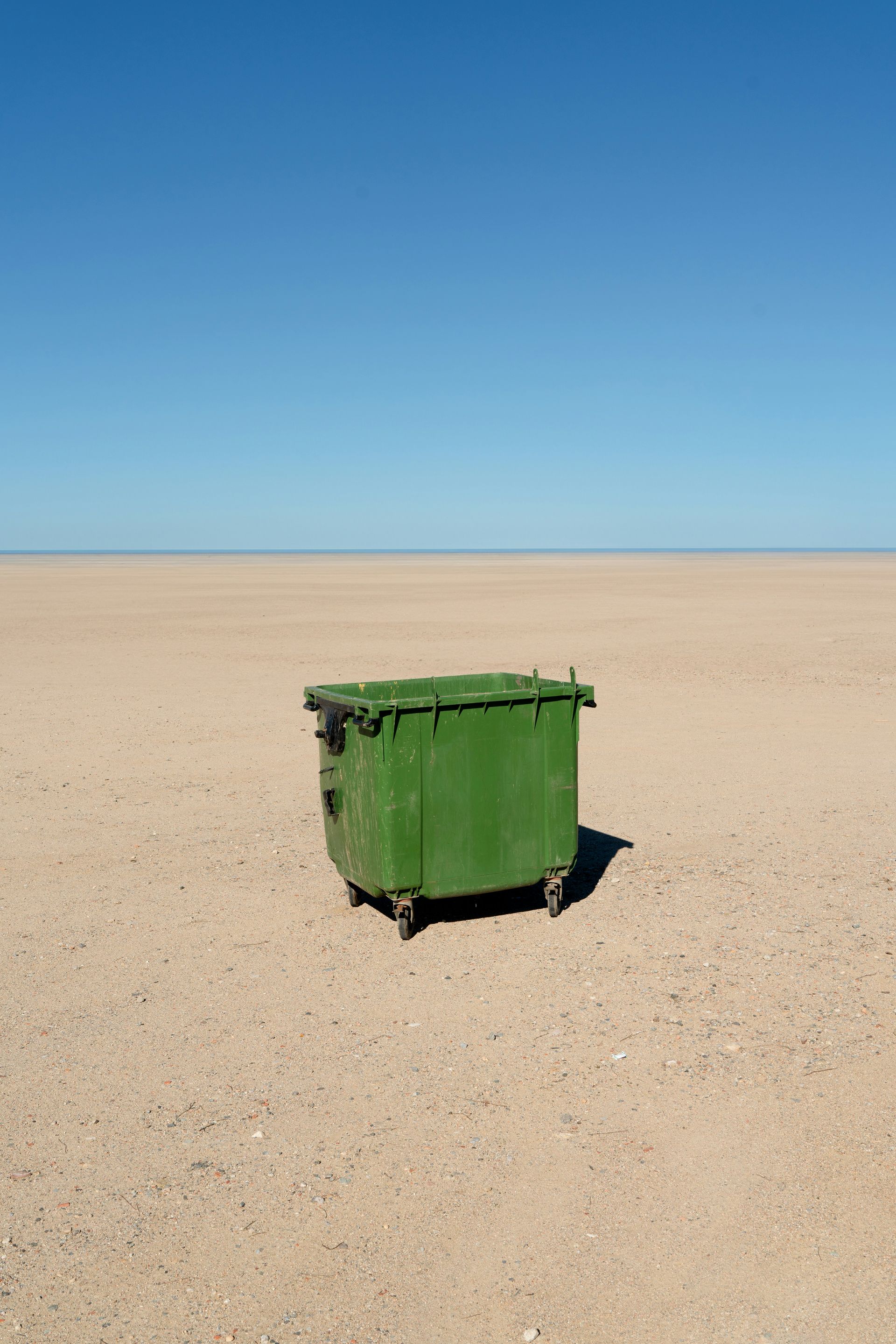 A green dumpster sits alone in the desert.